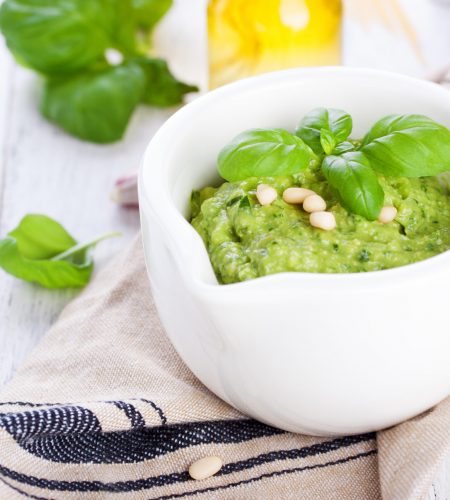 Homemade traditional basil pesto with olive oil, cedar nuts and garlic in a white bowl on a wooden rustic table, closeup